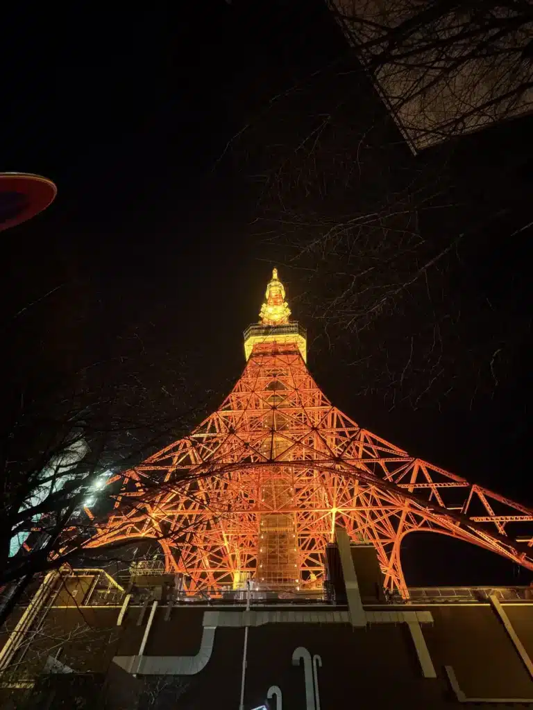 由塔底正下方垂直仰望東京鐵塔,橘色的幾何鋼鐵結構在黑夜中交織成細密的網格。