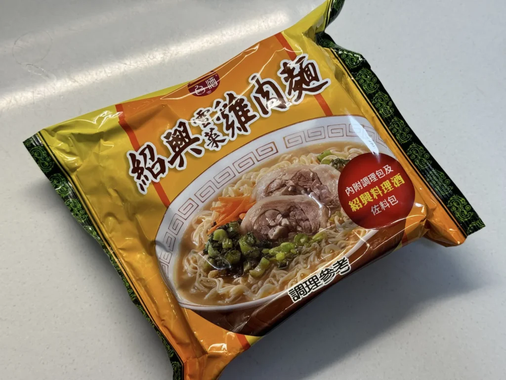 台酒紹興雪菜雞肉麵的外包裝袋，橘色包裝印著紹興雪菜雞肉麵