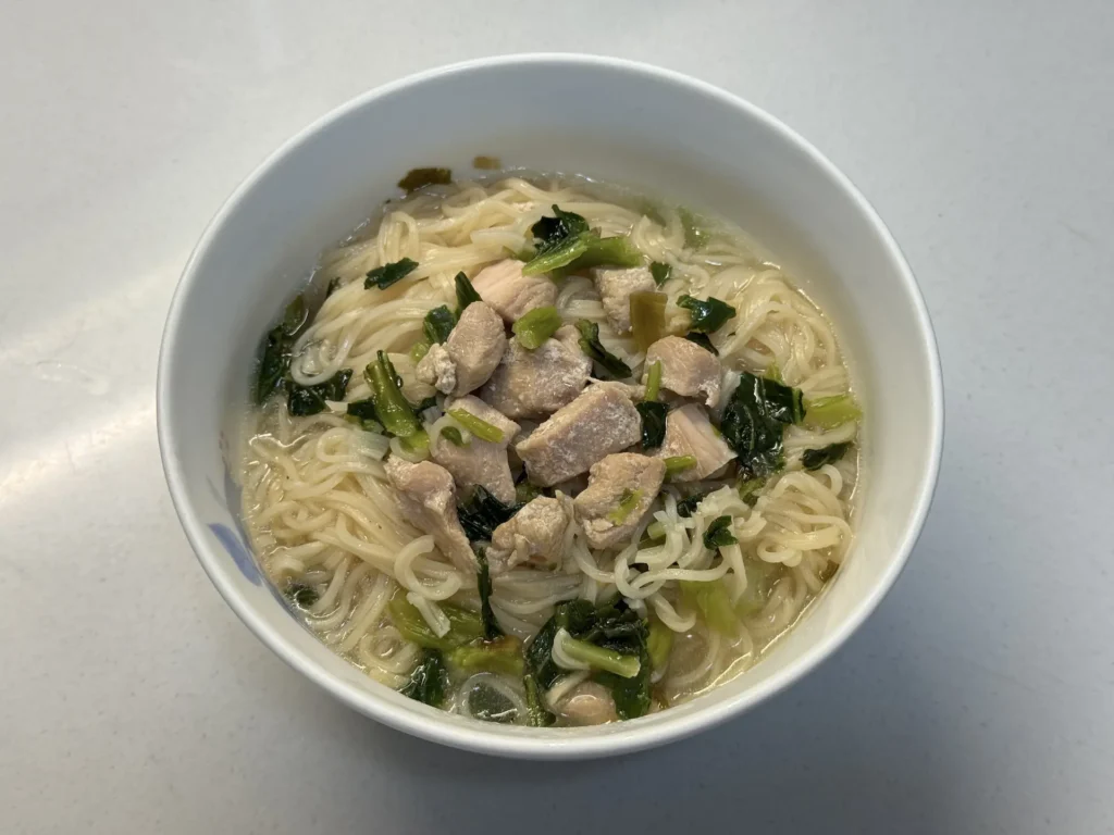 煮好的台酒紹興雪菜雞肉麵，麵條與雞肉青菜盛在白碗裡