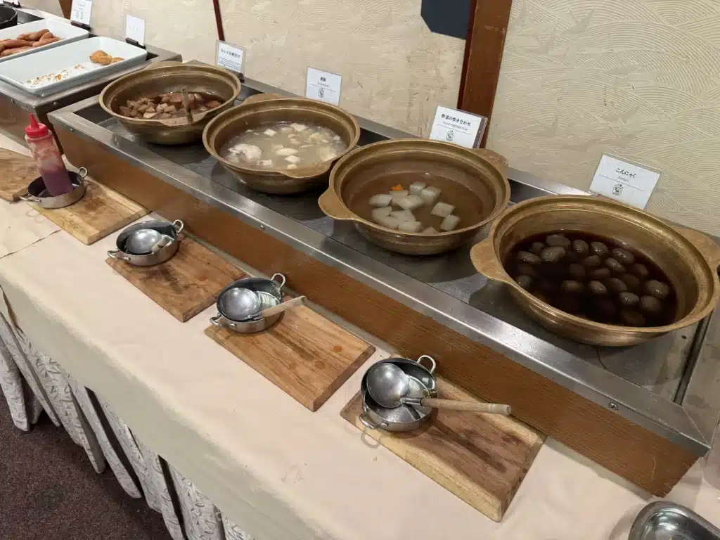 湯澤東映飯店早餐區的燉煮料理檯，包含蒟蒻、白蘿蔔、煮豚、紅鰈魚煮付け等熱食，大鍋分別放置在保溫台上。