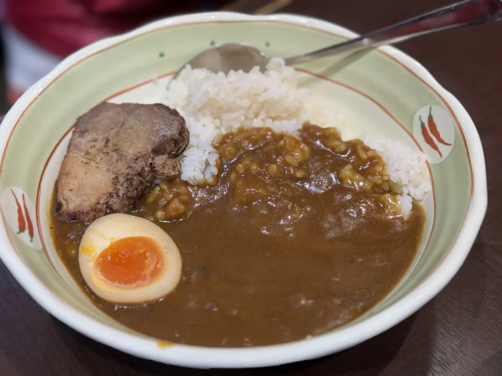 一碗日式咖哩飯，上面放著叉燒與半顆溏心蛋，白飯與咖哩醬分側擺放。