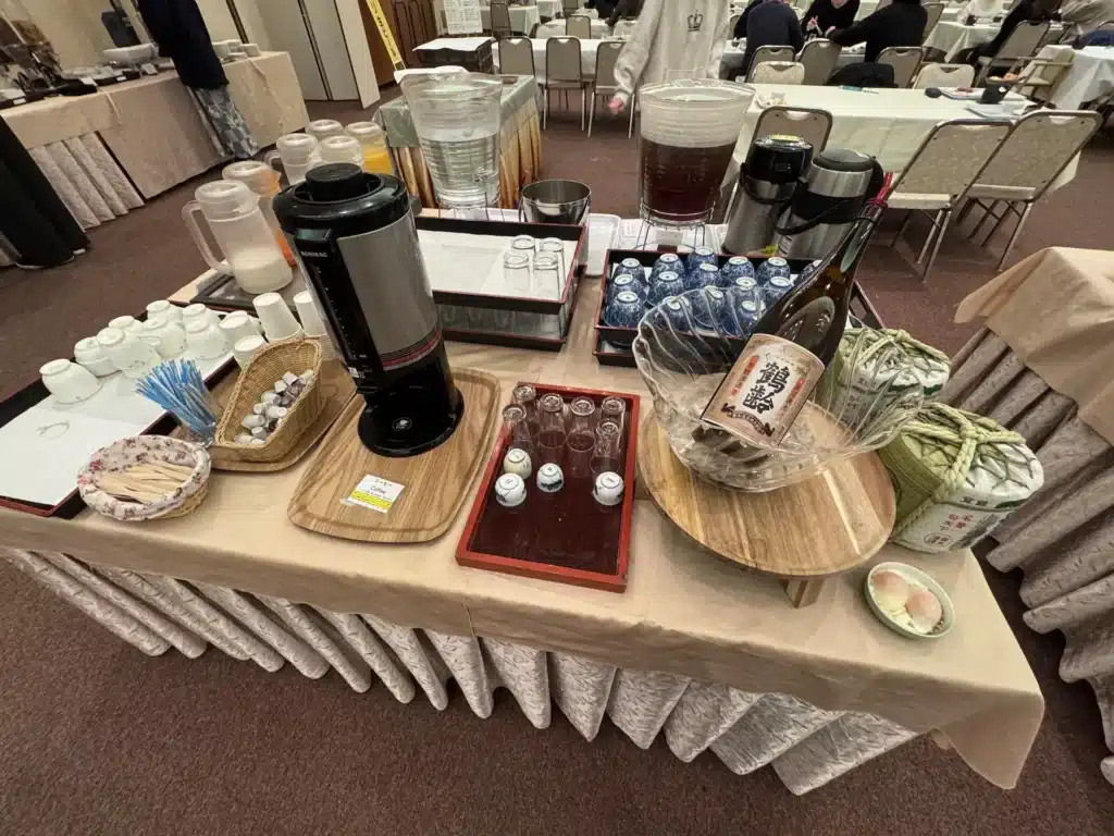 湯澤東映飯店早餐飲品區，擺放咖啡機、果汁、冰水、熱茶，以及一瓶提供試飲的清酒。