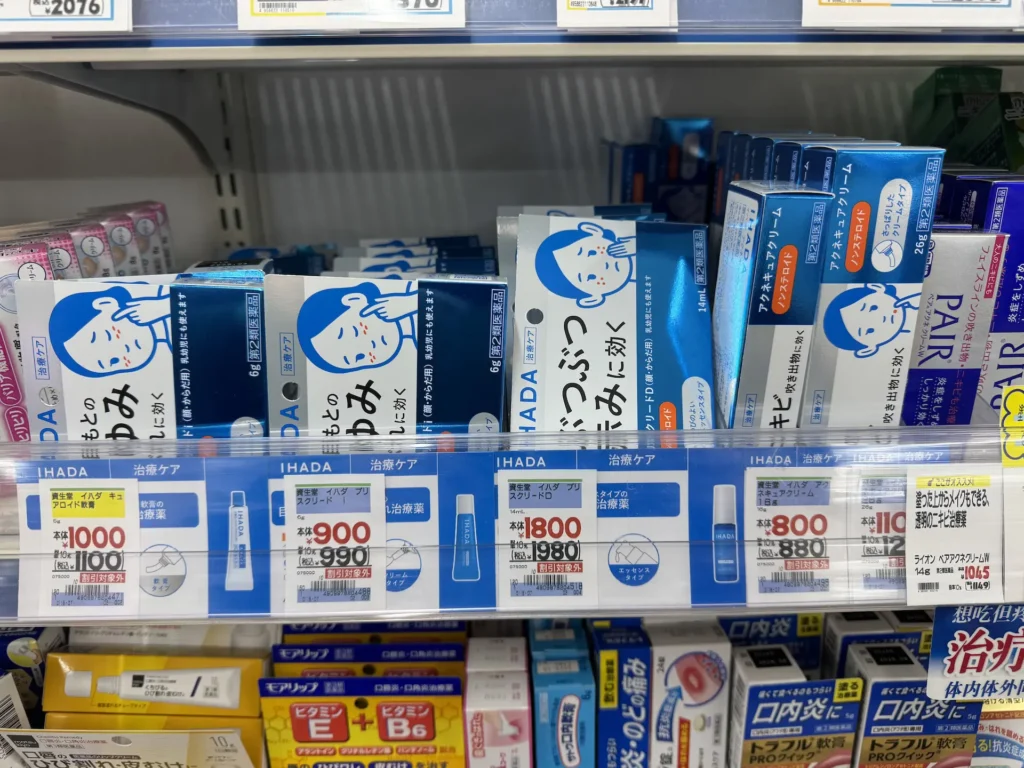 日本藥妝店貨架上陳列多款 IHADA 皮膚治療用品，包含針對過敏、紅腫、濕疹與皮膚搔癢的藥膏與乳霜，商品標示清楚並附上價格牌。