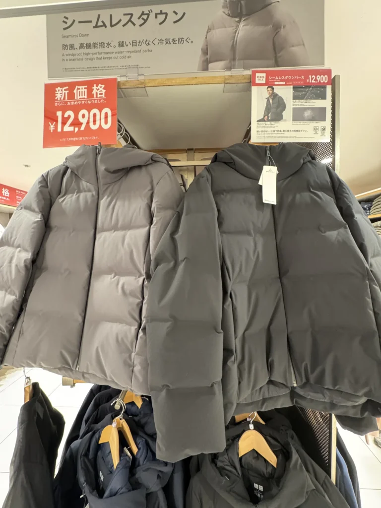 Uniqlo 店內展示架上,兩件無縫羽絨外套掛在衣架上,標示特價 12,900 日圓。