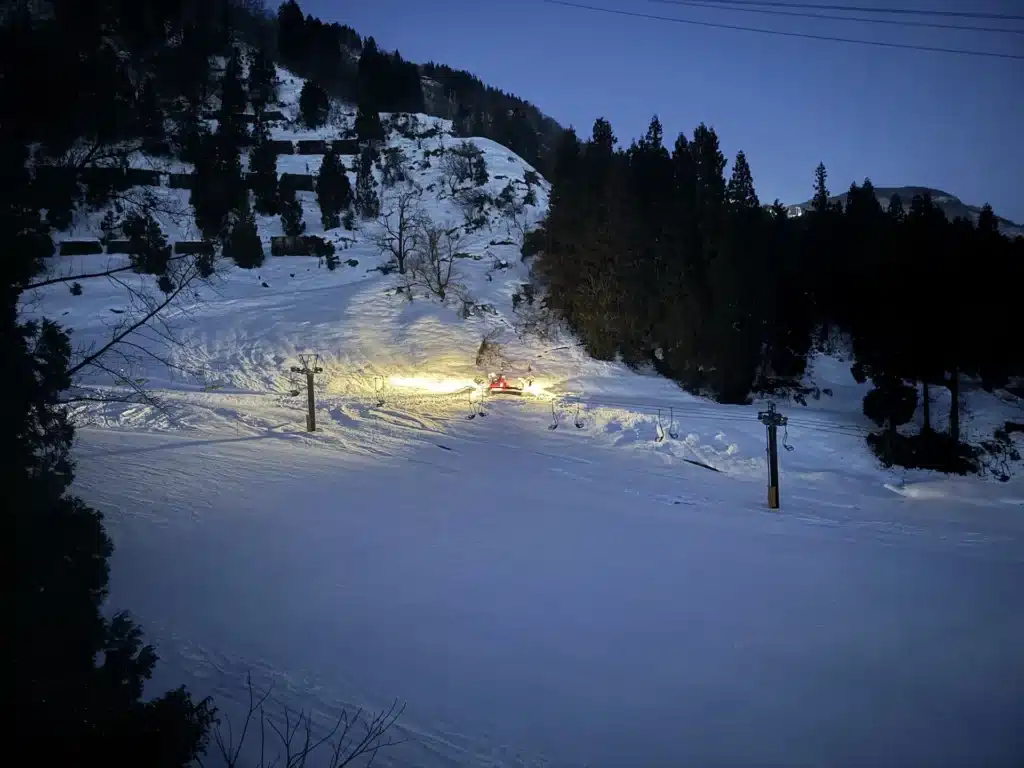 早上五六點,在遠方一台亮著強光的整地車在雪地上作業,四周被森林與山坡包圍。