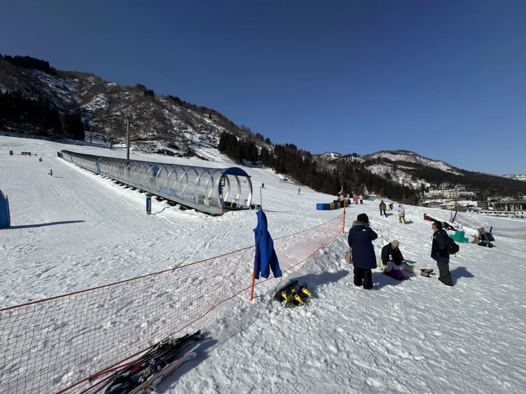 湯澤中里雪場的魔毯輸送帶與緩坡區,旁邊有家長與小孩在雪地活動。