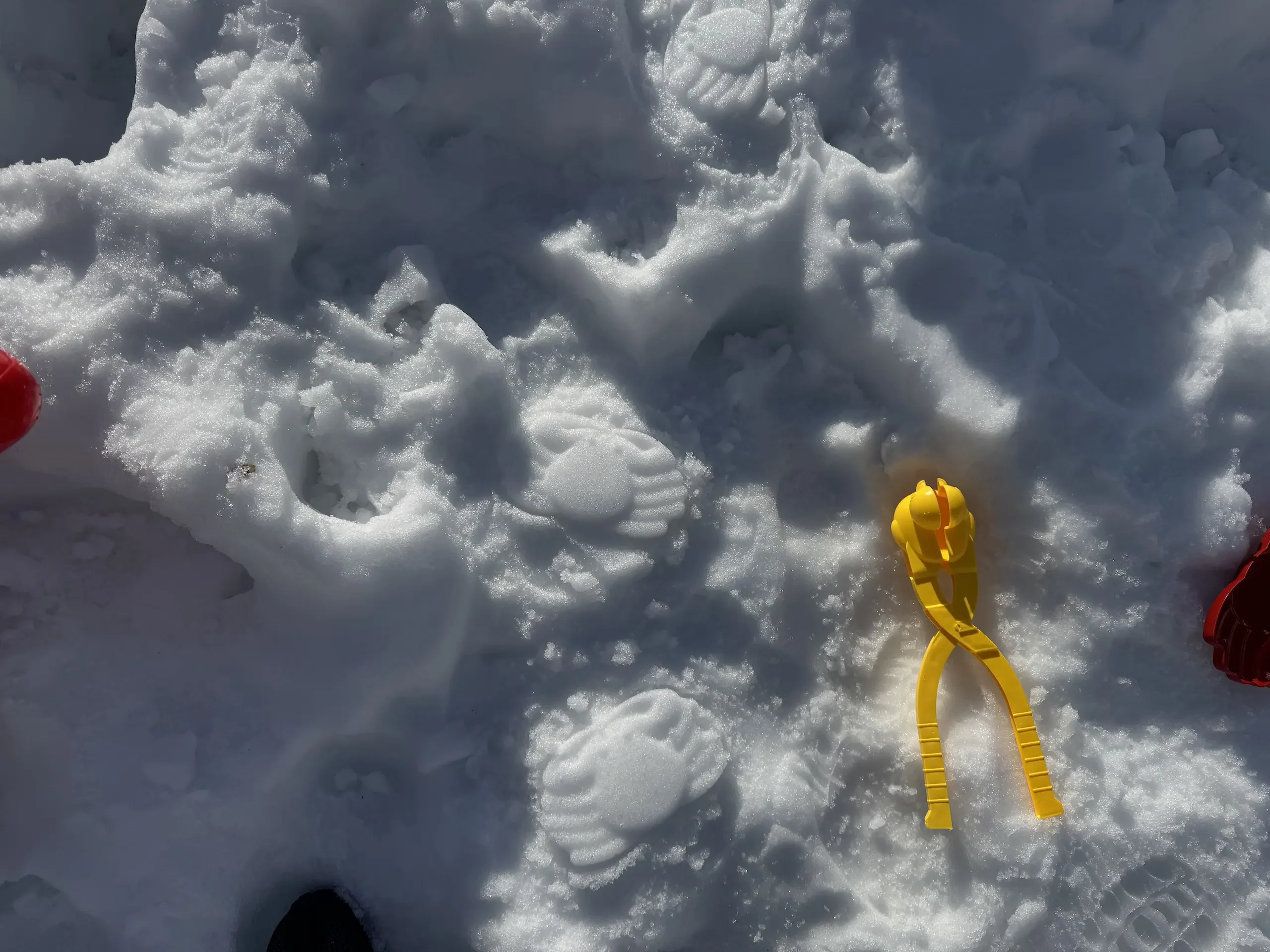 雪地上放著黃色雪夾與壓出的雪印,周圍可見小孩玩雪留下的腳印與痕跡。