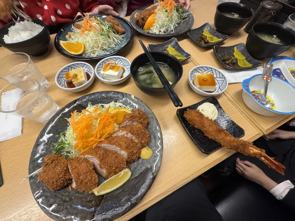 越後湯澤的「越後とんかつ人参亭」桌上擺滿多份豬排定食、炸蝦、味噌湯、小菜與白飯。