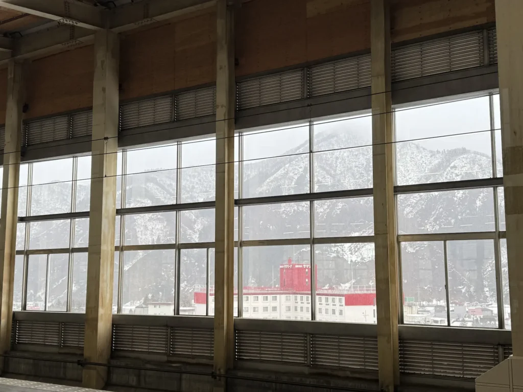 越後湯澤車站內透過大面積窗戶看到的雪山與城鎮建築,窗框排列整齊。