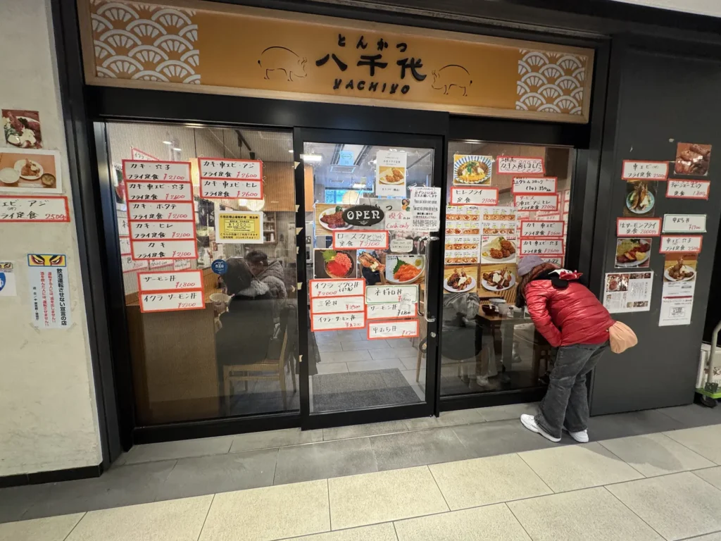 豐洲市場的とんかつ八千代店面外觀,玻璃門上貼滿當日料理與價格。