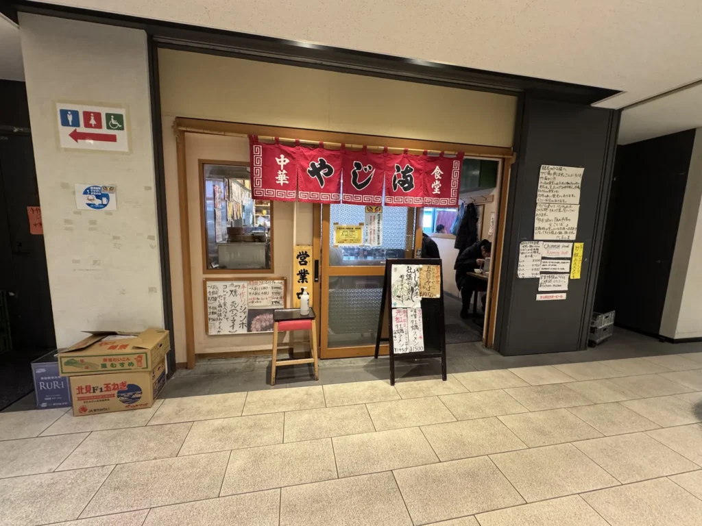 中華食堂やじ満店面外觀,紅色布簾與手寫菜單張貼在牆上。