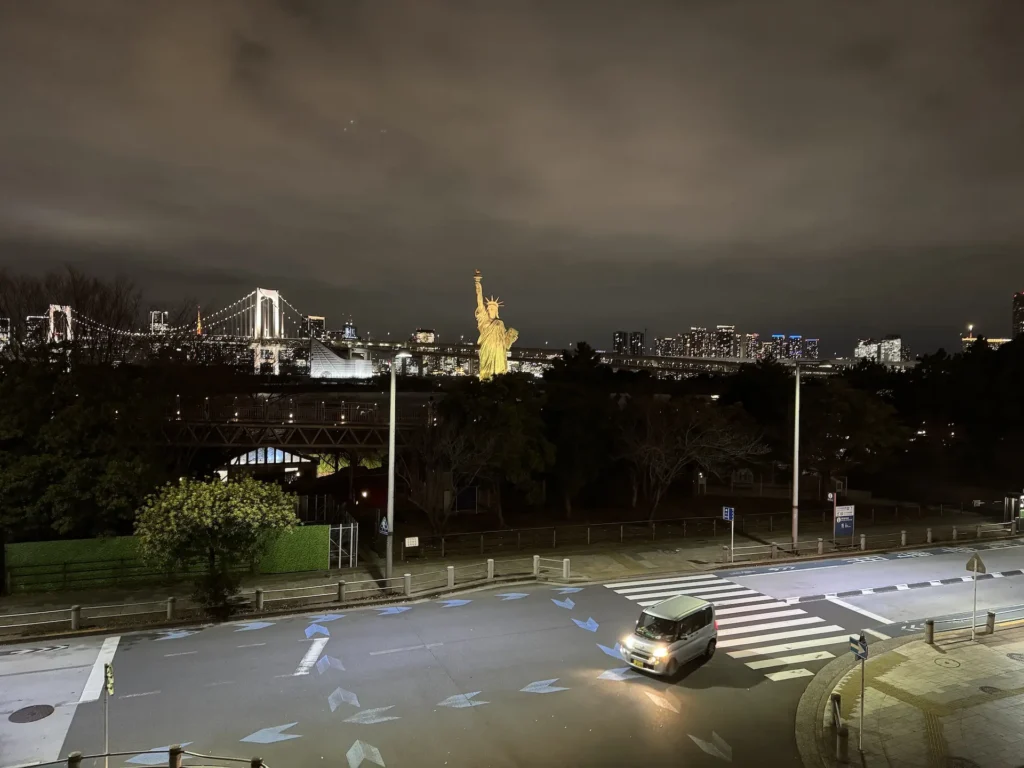 台場夜景遠眺彩虹大橋與自由女神像,前景是馬路與一台行駛中的小車
