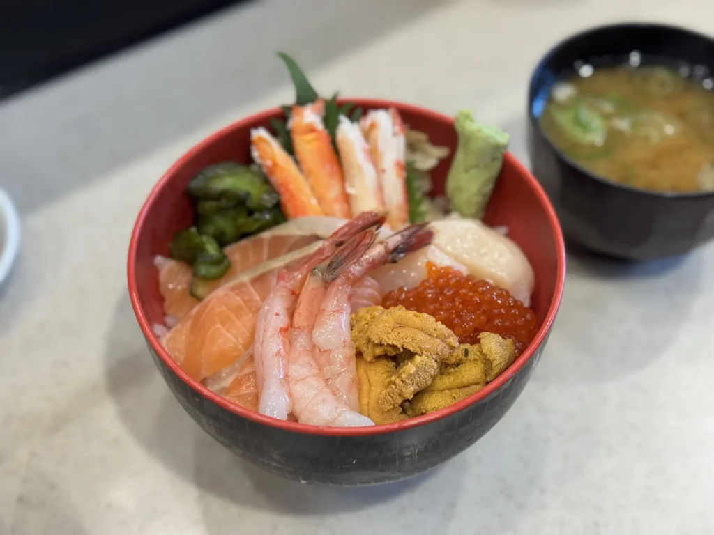 北海道三味丼特寫,內含鮭魚、甜蝦、海膽、鮭魚卵、干貝、螃蟹腳與小黃瓜,旁邊附味噌湯