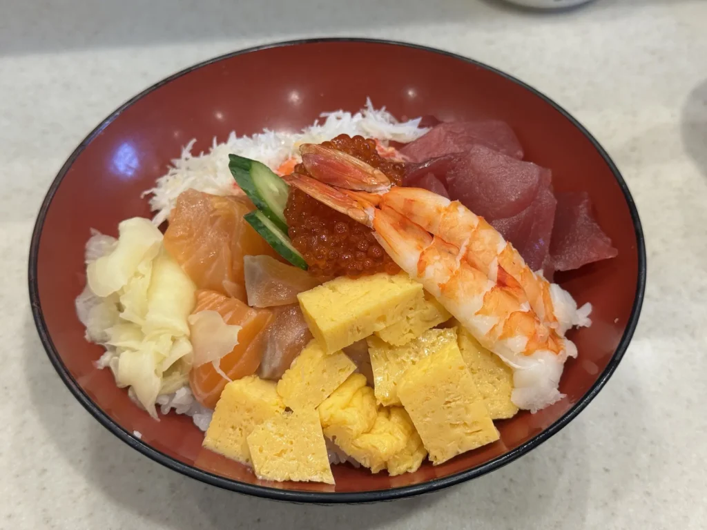 玉子燒丼飯特寫,包含鮭魚、鮪魚、甜蝦、玉子燒、鮭魚卵與薑片。