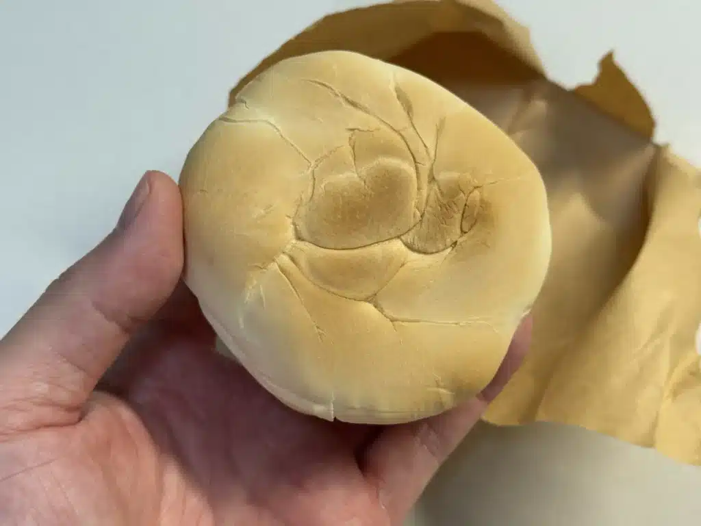 一隻手拿著一個完整、圓扁狀的「吉家槓子頭」。槓子頭表面呈現淺金黃色，帶有老麵自然發酵後形成的皺褶和細微裂紋，呈現紮實的質感。