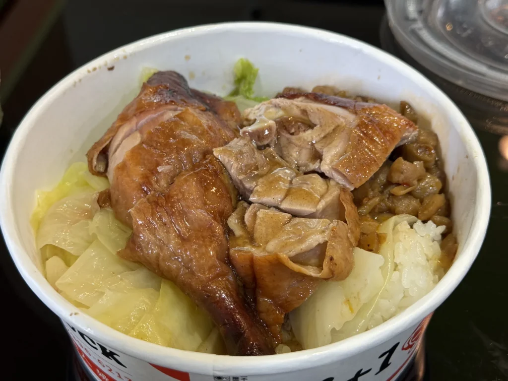 1+1 燒臘烤鴨腿飯打開，一整隻鴨腿放在白飯和高麗菜上