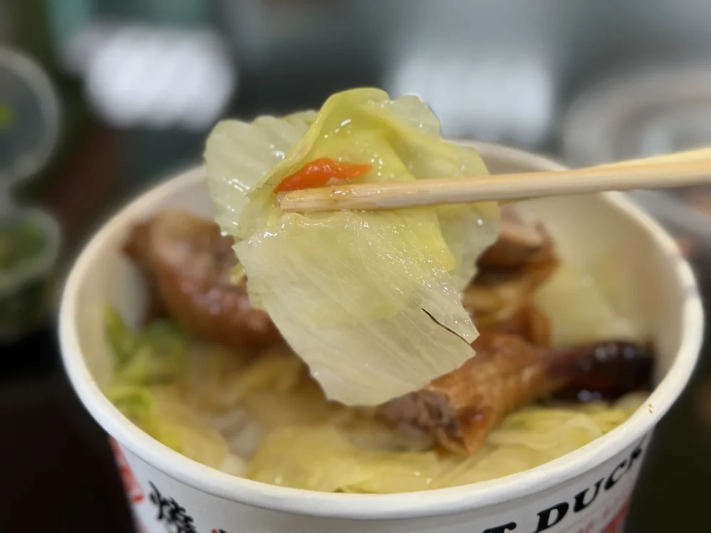 筷子夾起 1+1 燒臘便當裡的高麗菜