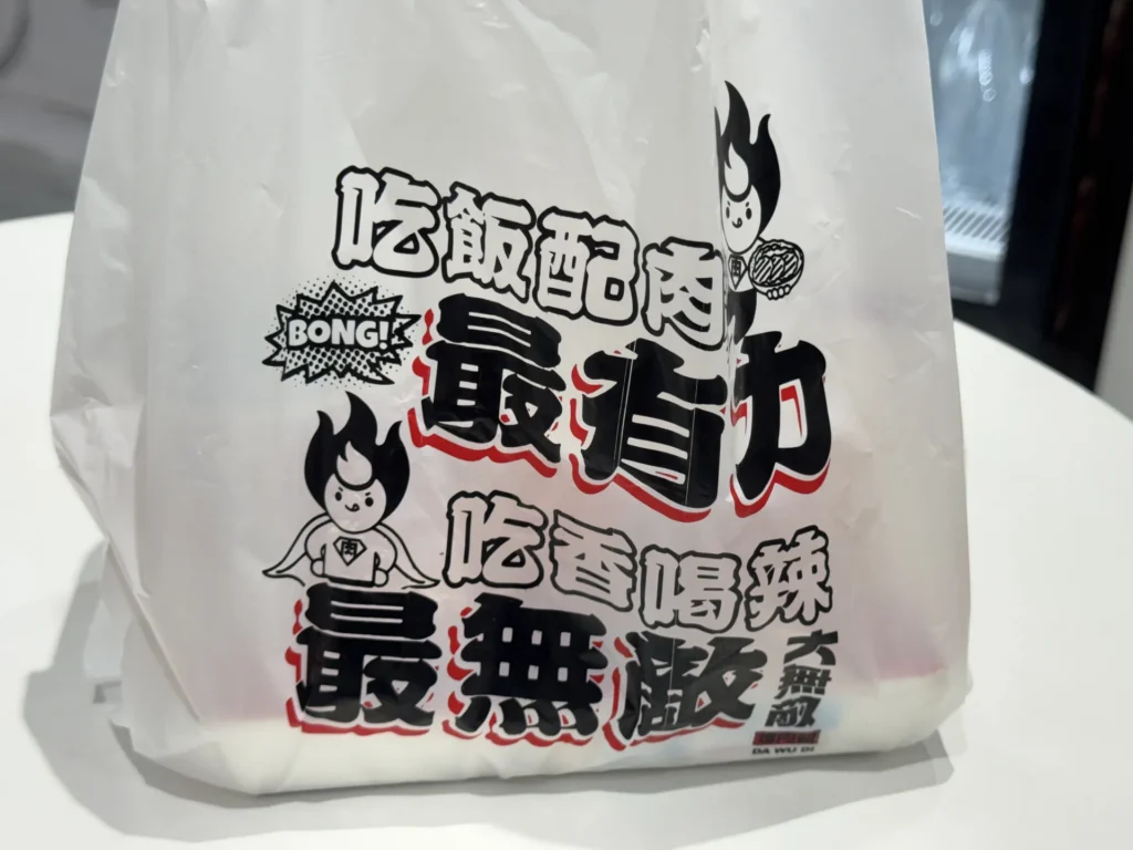大無敵烤肉飯中正南昌店的外帶袋,印著吃飯配肉最有力、吃香喝辣最無敵