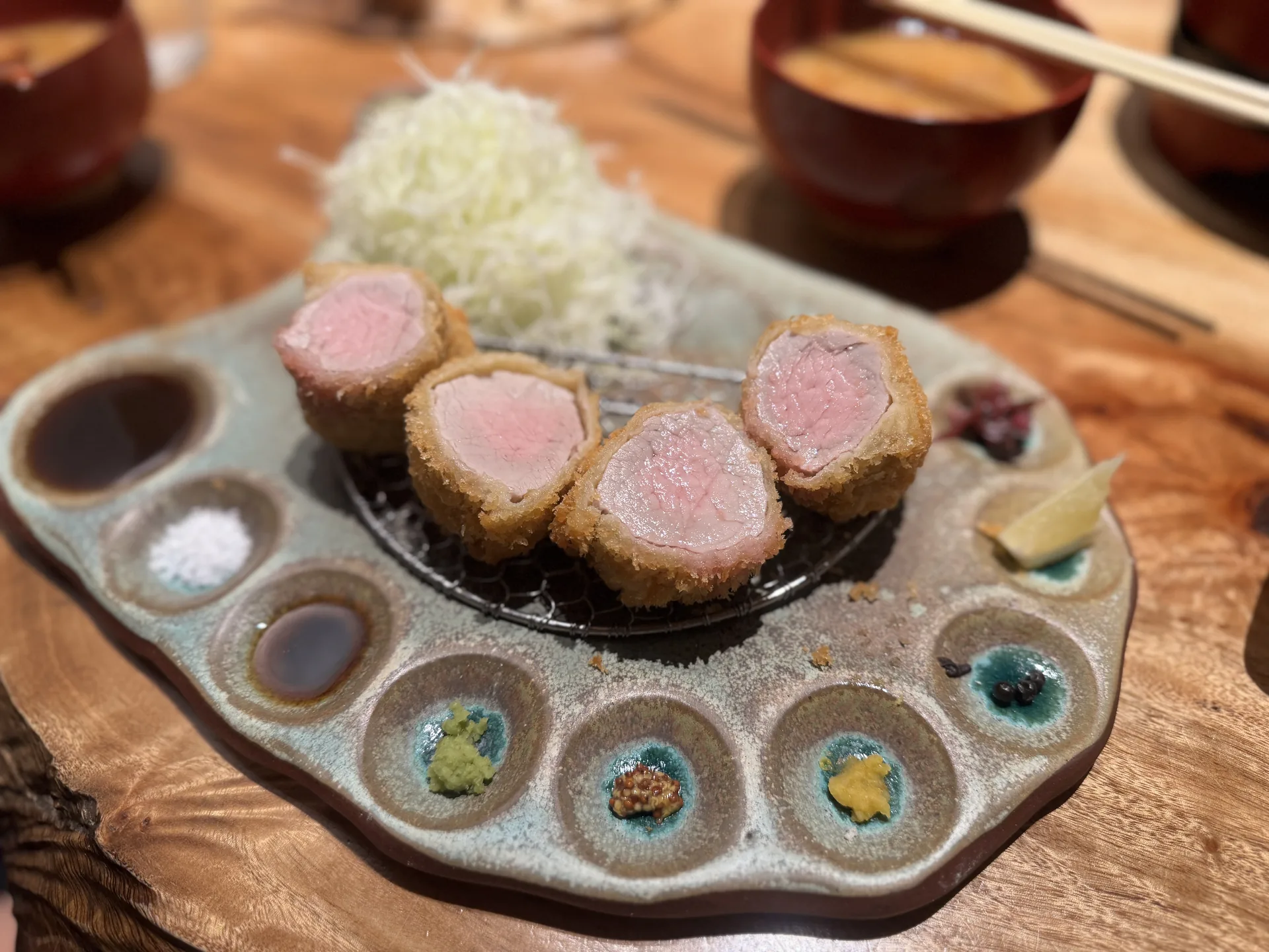 日式炸牛排切面粉嫩，搭配多種沾醬、鹽與高麗菜絲的定食擺盤