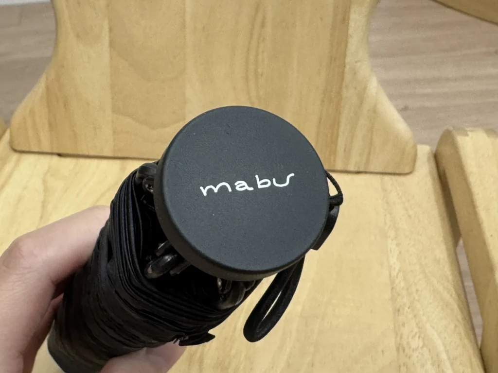 手拿 mabu 雨傘，傘柄尾端印著 mabu 字樣，附一條手繩