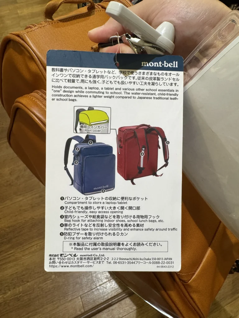 montbell書包吊牌背面的功能說明,列出平板夾層、大開口、掛鉤、反光條與防身警報器環