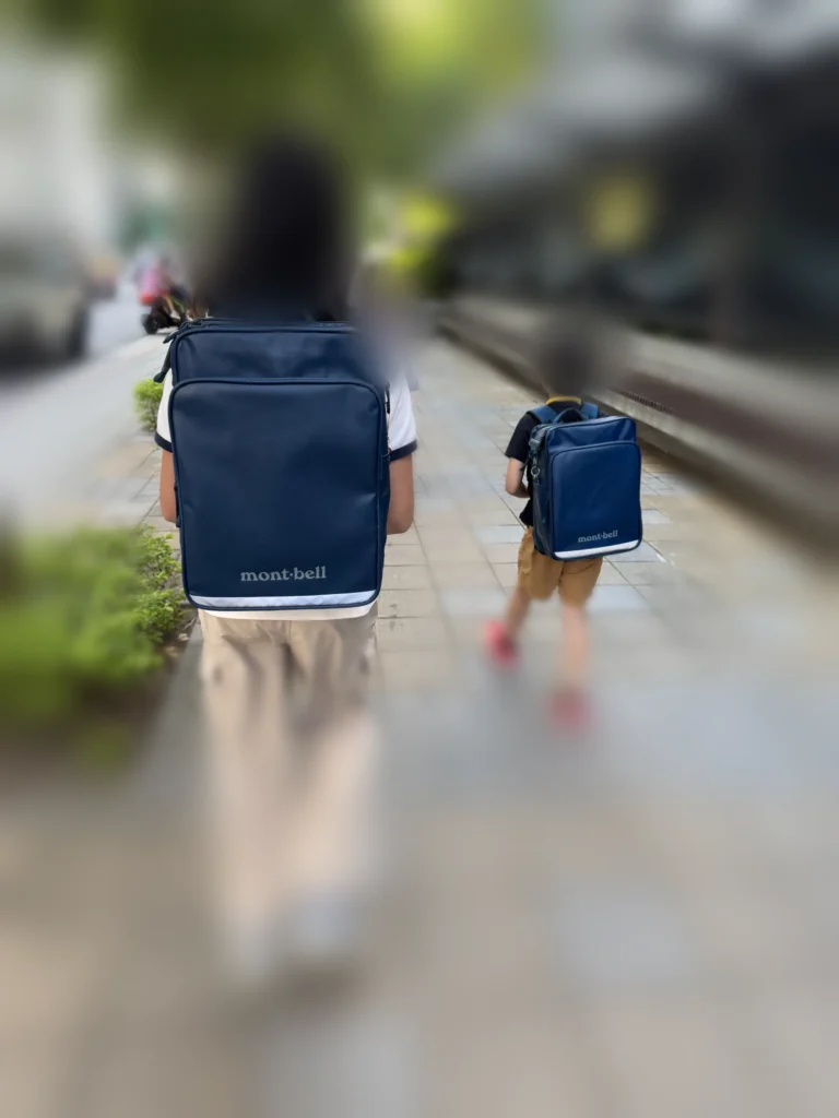 兩個孩子背著深藍色 montbell書包走在上學路上的背影