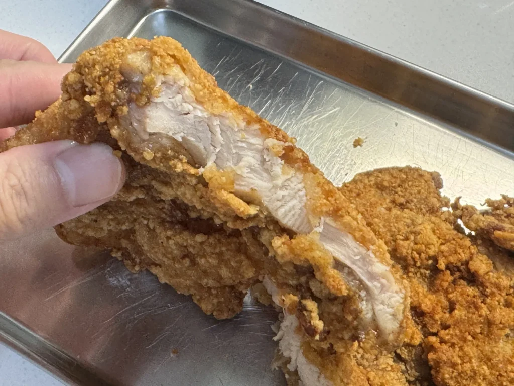 南機場夜市雞排用手撕開，露出厚實白嫩的雞胸肉，斷面帶著肉汁油光