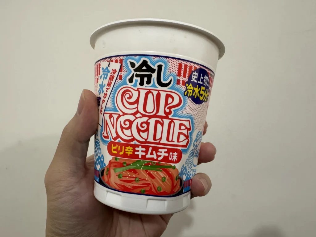 手拿日清冷水泡麵,杯身寫著冷しカップヌードル ピリ辛キムチ味