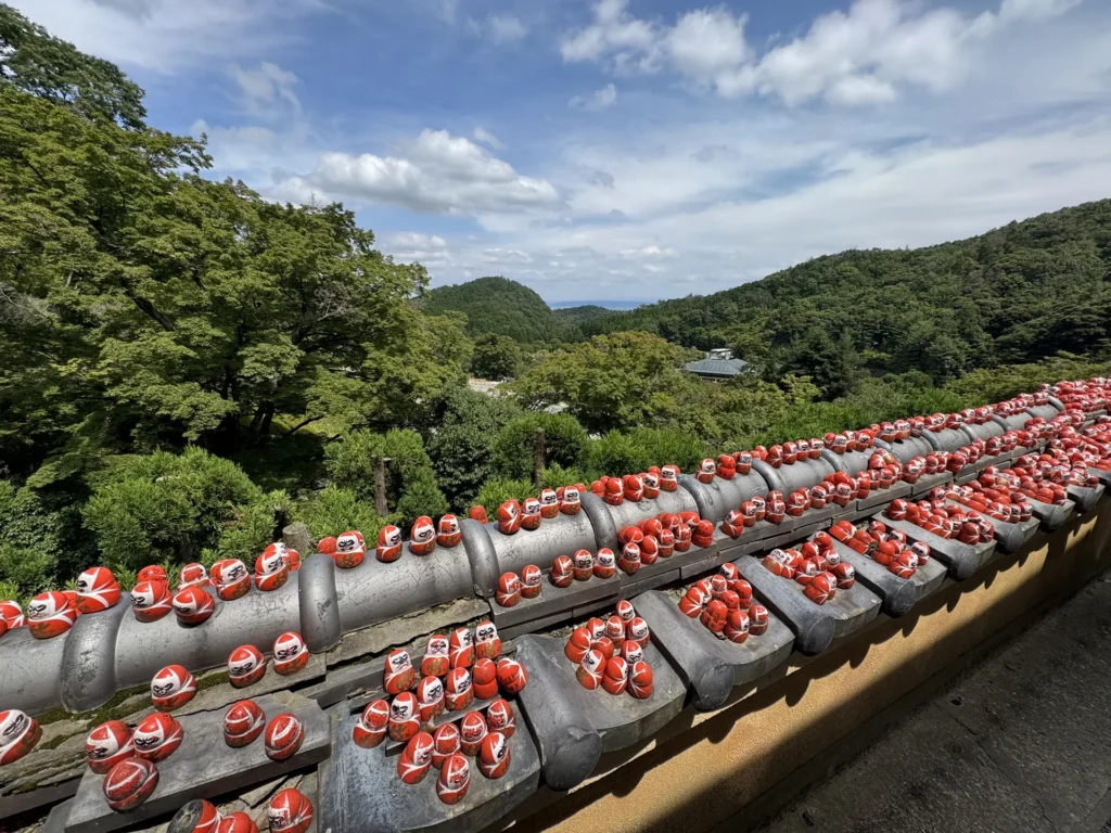 勝尾寺步道旁的矮牆上,擺滿一排排的小達摩,後面是山景
