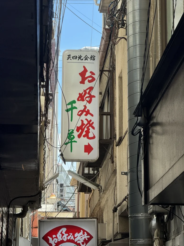 窄巷口的招牌，寫著お好み焼 千草，箭頭指向巷子裡
