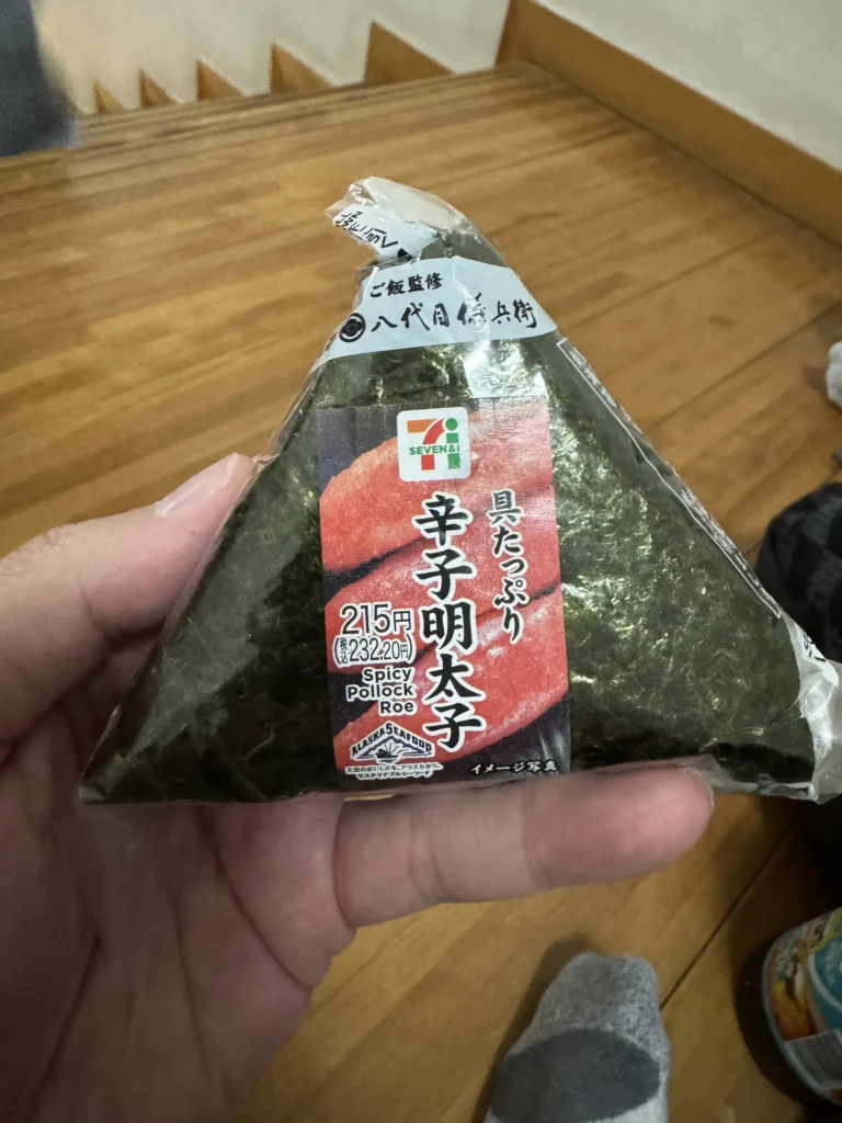 手上拿著 7-11 的辛子明太子飯糰,215 日幣