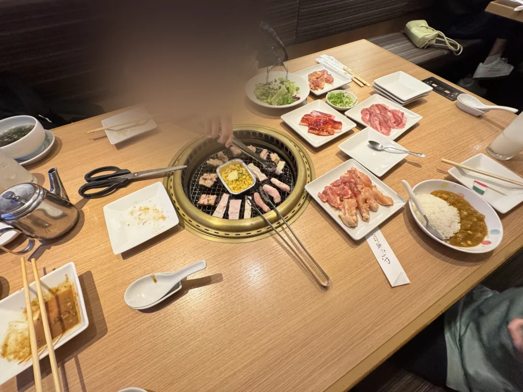 燒肉桌上擺滿了肉盤、沙拉和咖哩飯，中間是烤網