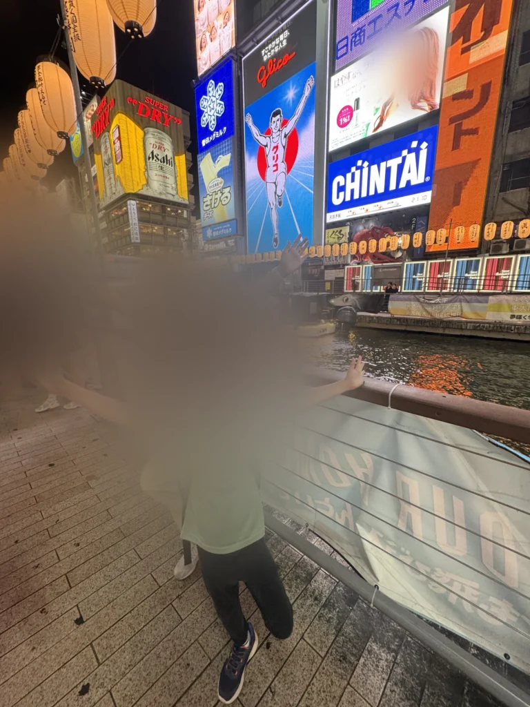 道頓堀的跑跑人看板前，小孩張開雙手擺姿勢
