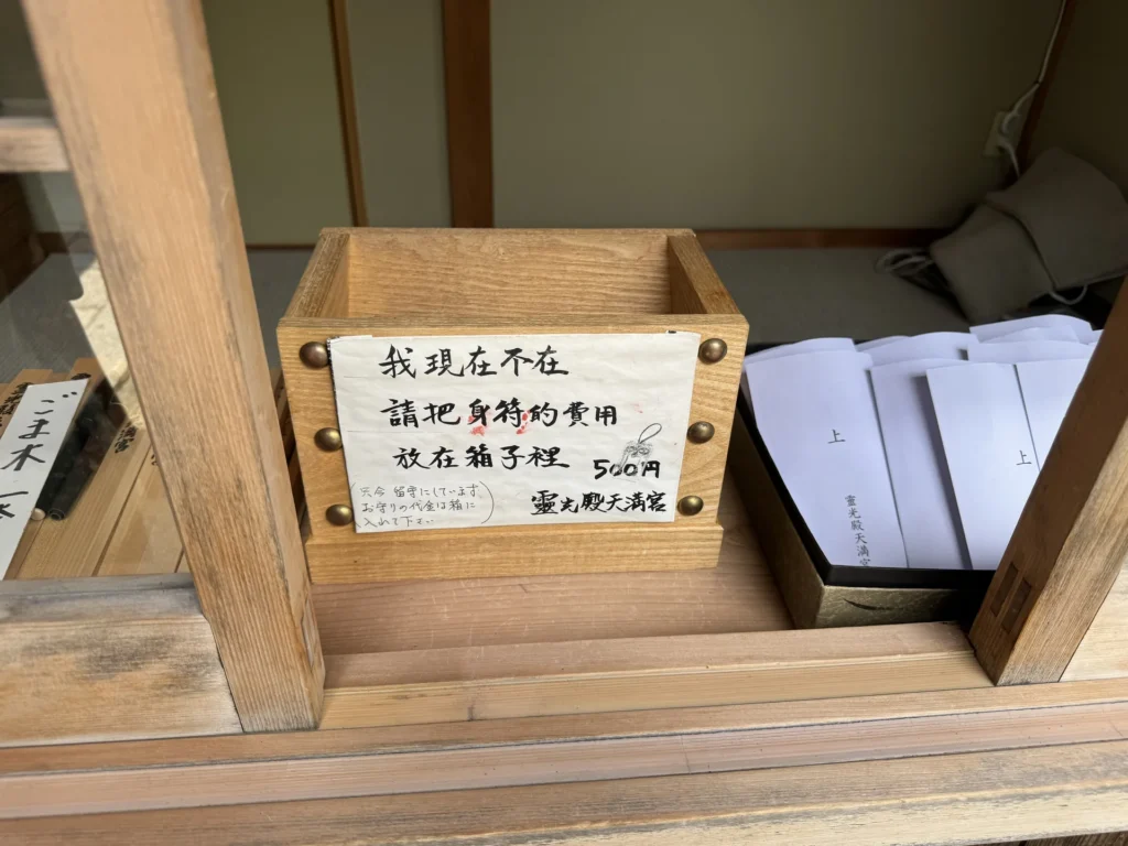 靈光殿天滿宮授與所的箱子，中文紙條寫著我現在不在，請把身符的費用放在箱子裡，500 円