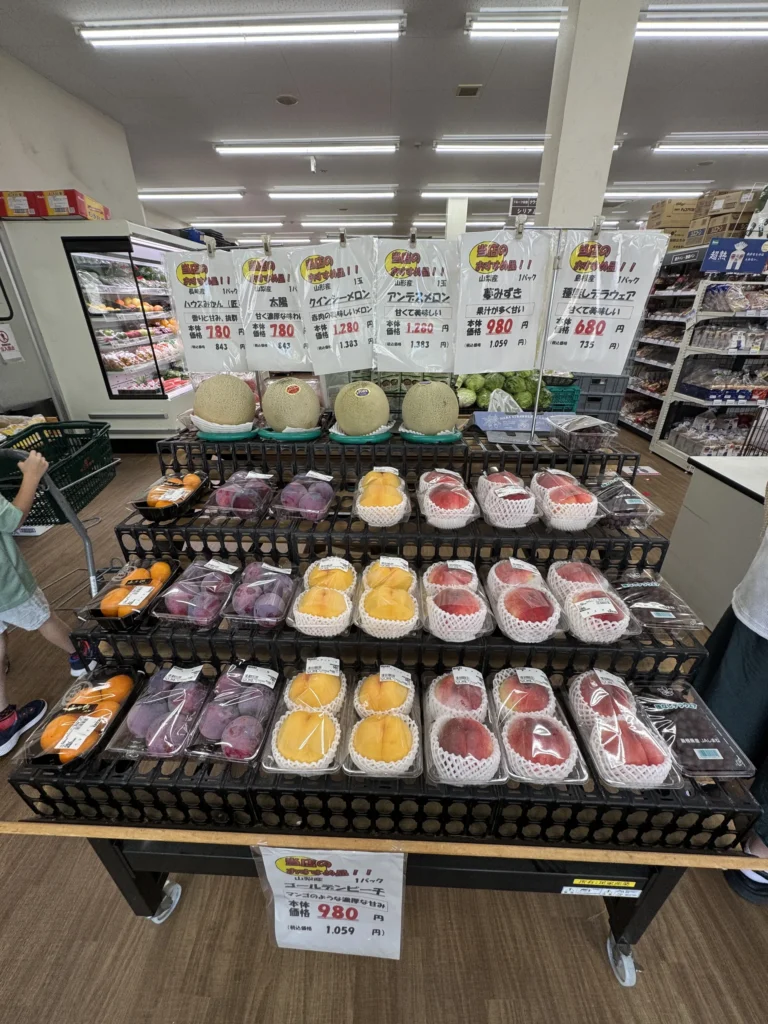 超市入口的水果架，擺著哈密瓜、黃桃和水蜜桃