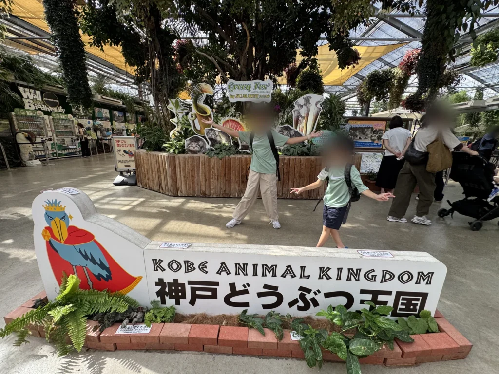 神戶動物王國的看板，旁邊是室內溫室裡的植物和遊客
