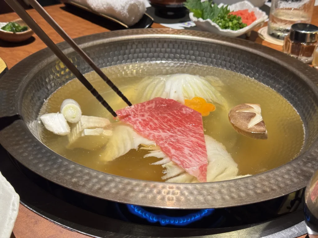 涮涮鍋裡涮著牛肉片，旁邊有白菜和香菇