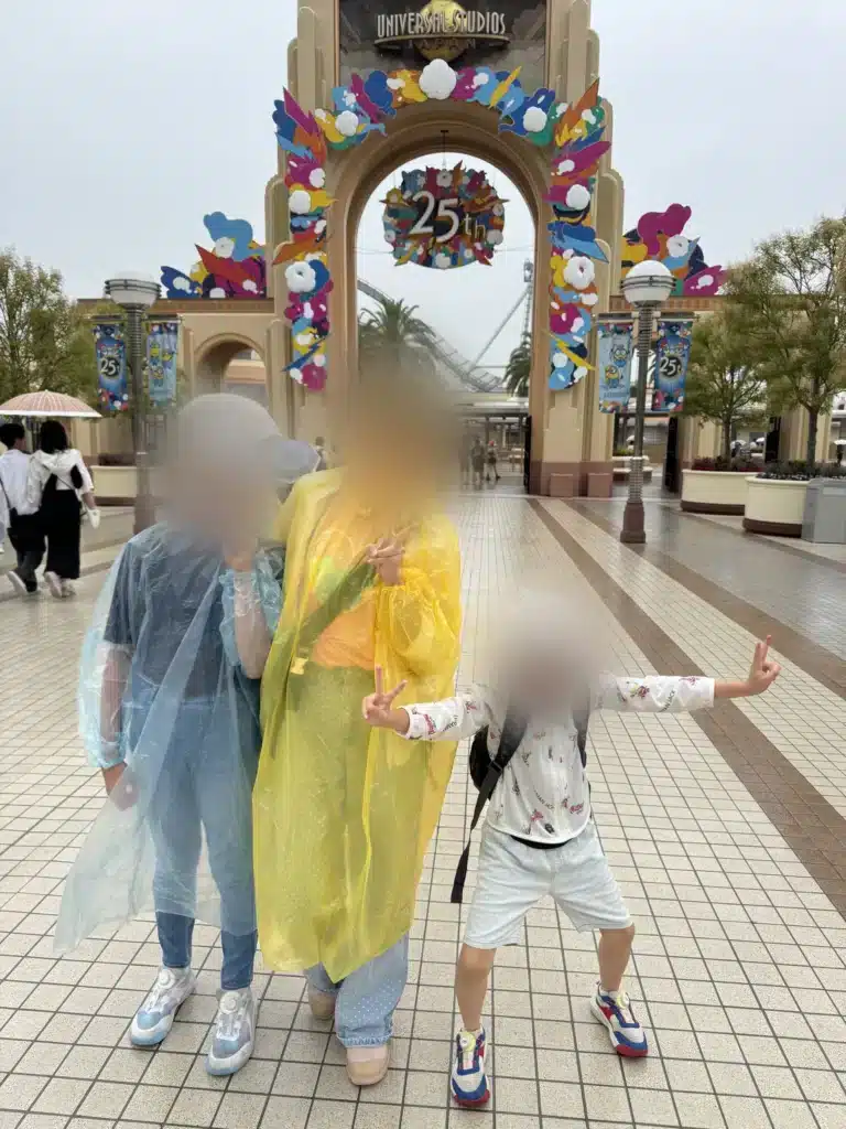 環球影城 25 週年入口拱門前，一家人穿著雨衣合照